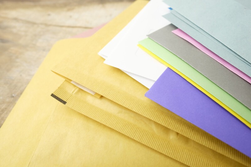 A stack of different coloured envelopes against a wooden surface.