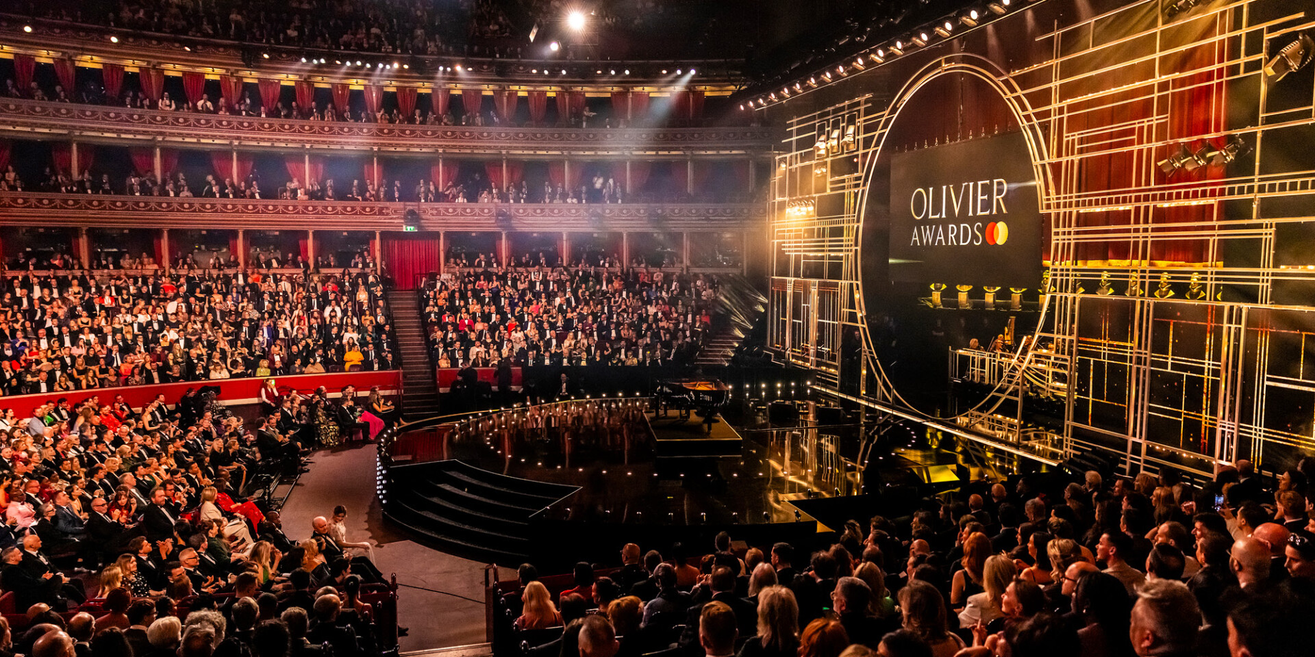 A packed audience at the Royal Albert Hall during the Olivier Awards ceremony, with the stage illuminated by golden lighting.