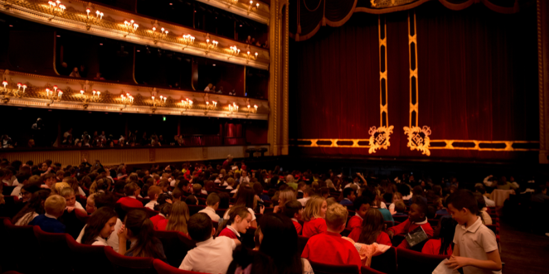 Photo of school pupils sat in stall seats at the Royal Opera House, preparing to watch Swan Lake Schools' Matinee © 2022, the image shows the opera stage and balcony seats. (Photo graph Rachel Cherry)